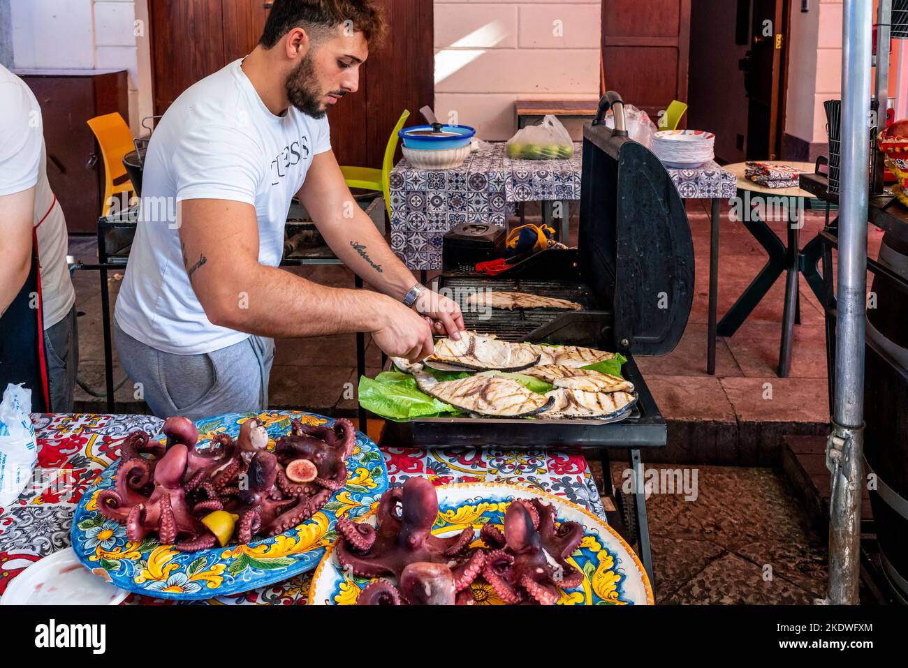 A Young Man Cooking Fish On A Grill At The Ballaro Street Market, Palermo, Sicily, Italy. Stock Photo