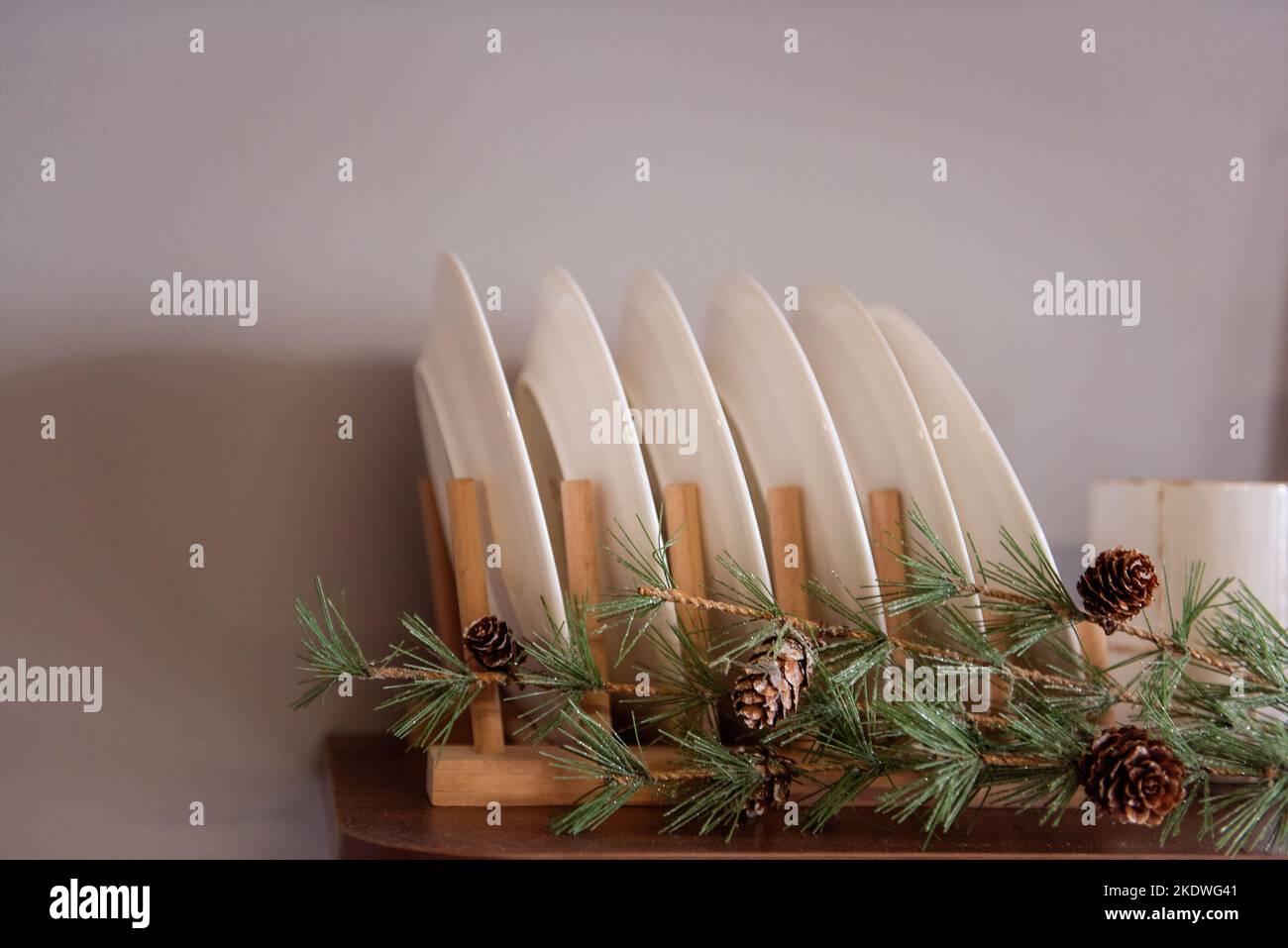 Stylish, concise Kitchen decoration for Christmas. Wooden shelves with plates, decorated with a garland and spruce branches. Fashionable minimalism in Stock Photo