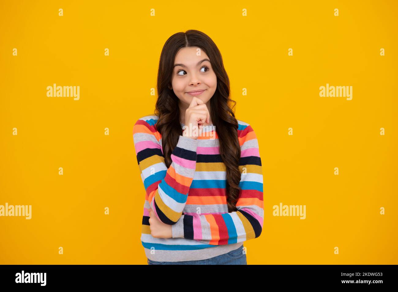 Happy teenager, positive and smiling emotions of teen girl. Thoughtful teenage child girl on yellow background. Portrait of a kid thinking over idea Stock Photo