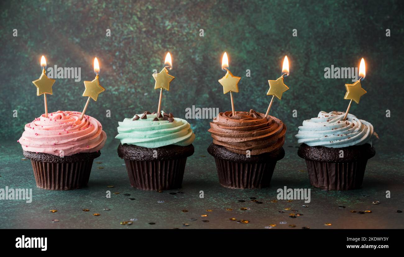 A row of cupcakes with gold star glowing candles, against a dark background. Stock Photo