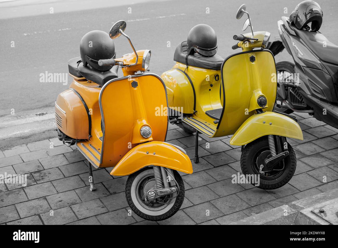 Yellow and orange vintage scooter motorcycle while the other objects are monochrome or black and white or desaturated Stock Photo