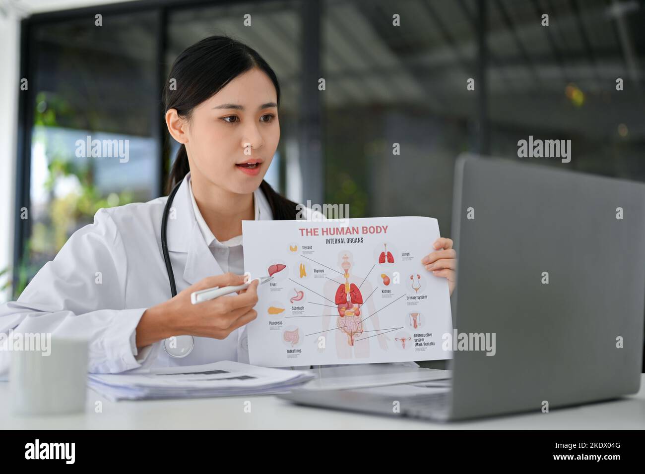 Professional young Asian female doctor explaining and sharing her medical opinion to online meeting's participants, having a medical webinar with her Stock Photo