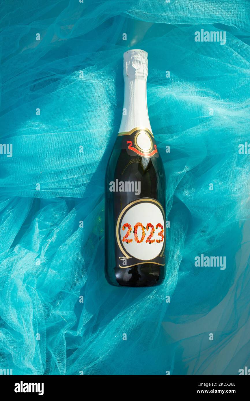 Champagne bottle with 2023 written on the label with orange roses font, on bright blue fabric waves, frat lay soft focus Stock Photo