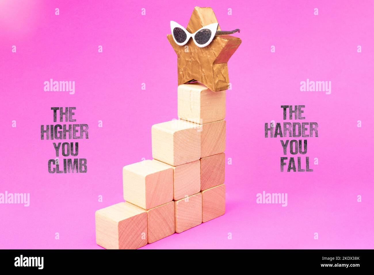The Higher You Climb the Harder You Fall, written with textured stamp letters, next to a golden star on top of stairs made from wooden blocks Stock Photo