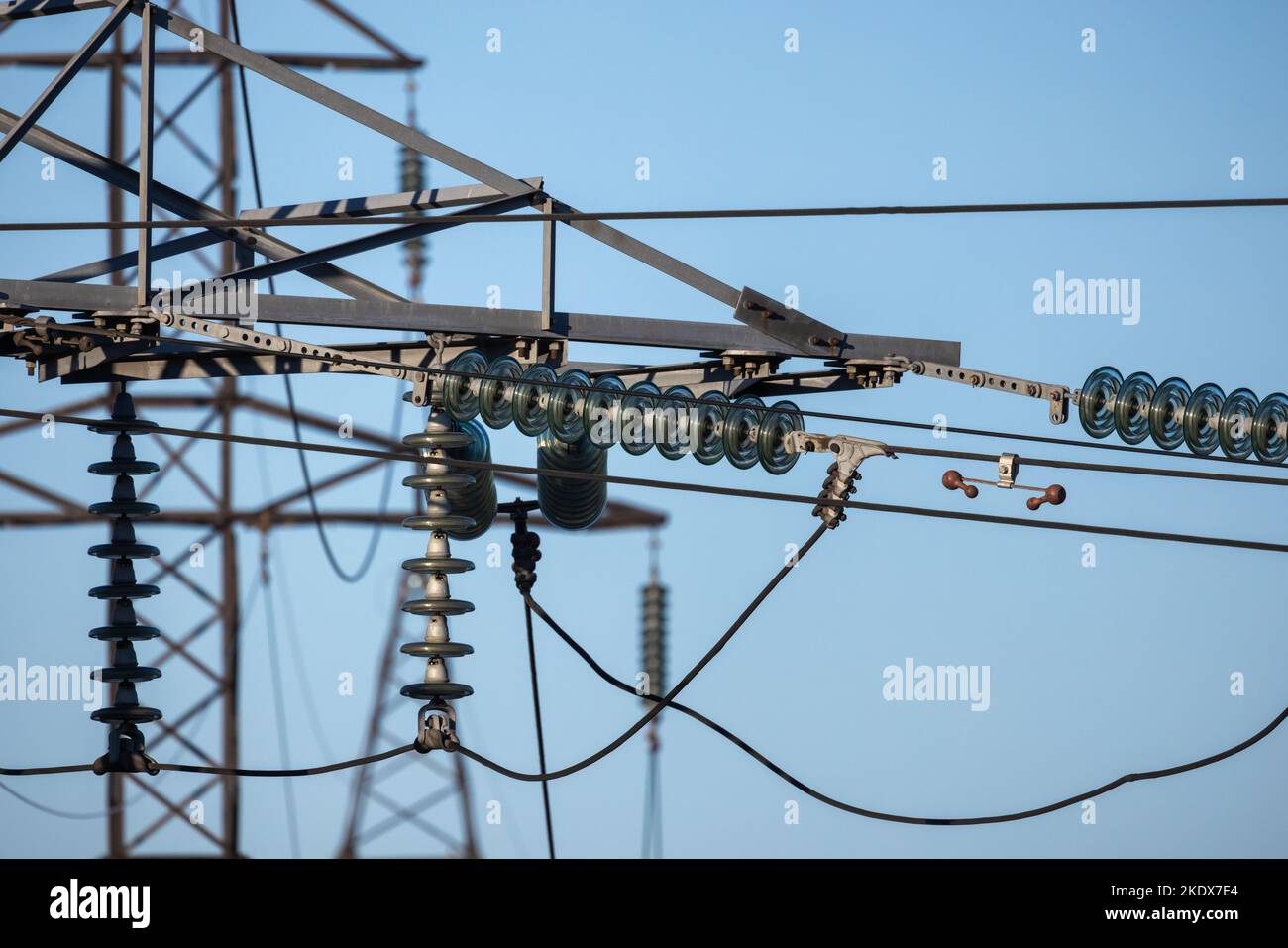 Insulators of high voltage overhead power lines are under blue sky on a daytime Stock Photo