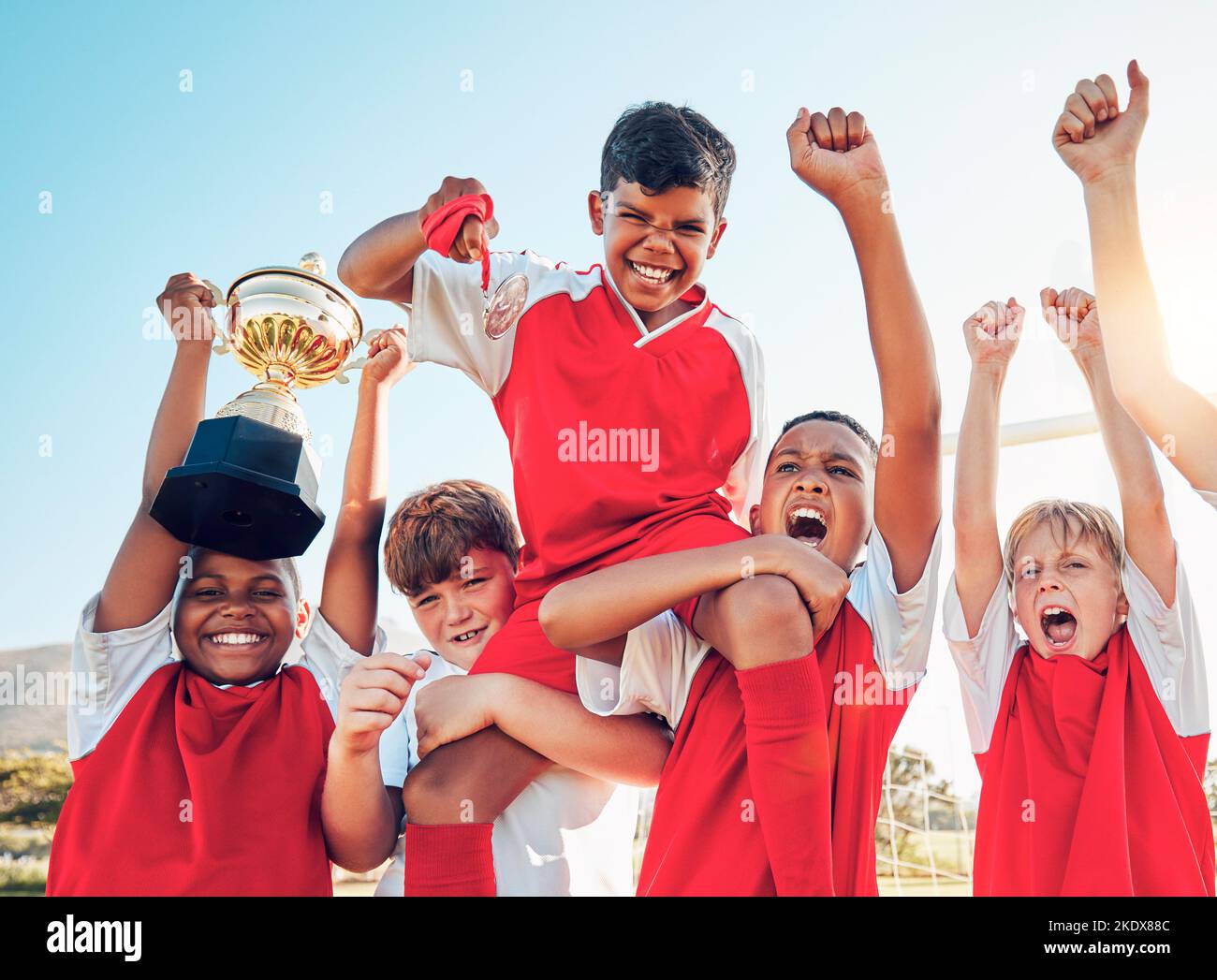 Soccer, celebration and kids team with trophy on soccer field, happy and excited at winning game. Sports, boy children goal and success in teamwork at Stock Photo