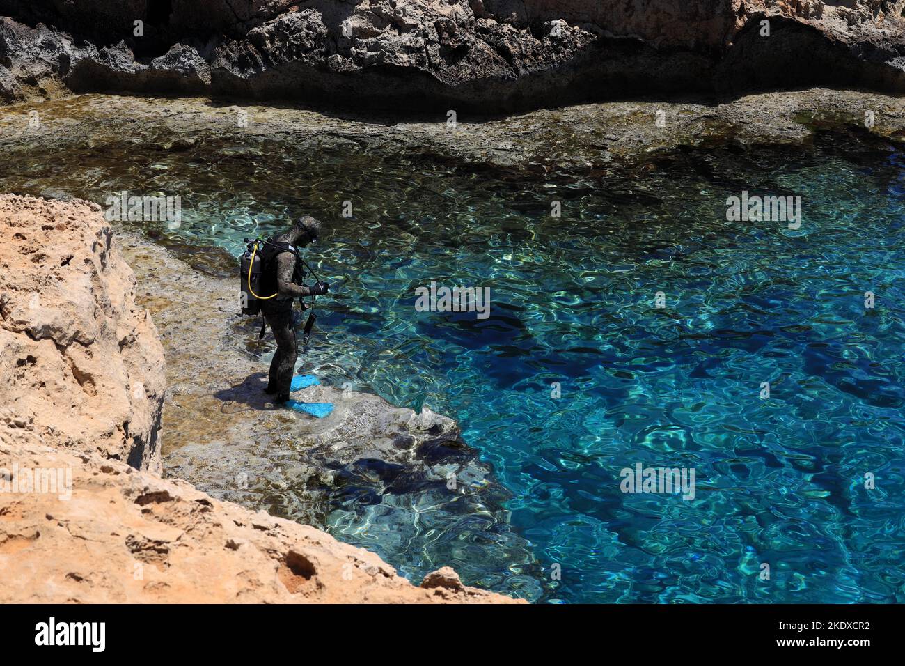 May 29, 2022, Larnaca, Cyprus: A scuba diver prepares to jump into the blue lagoon of the Mediterranean Sea at Cape Greco National Forest Park at the southern end of Famagusta Bay and forms part of Ayia Napa Municipality. The Republic of Cyprus stands at a historic and cultural crossroads between Europe and Asia. Its chief cities-the capital of Nicosia, Limassol, Famagusta, and Paphos have absorbed the influences of generations of conquerors, pilgrims, and travelers and have an air that is both cosmopolitan and provincial. Today Cyprus is a popular tourist destination for visitors from Europe, Stock Photo