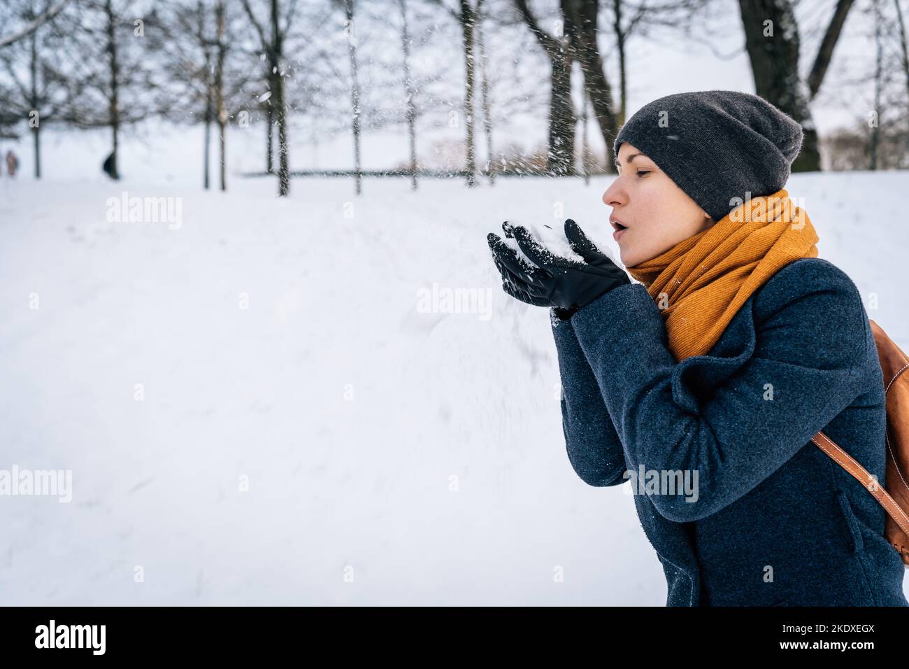 A woman in winter clothes blows snow off her palms in gloves. Stock Photo