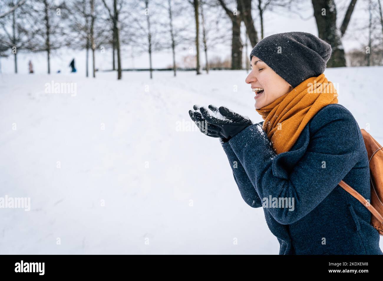 A young woman in warm winter clothes laughs looking at the snow in her palms Stock Photo