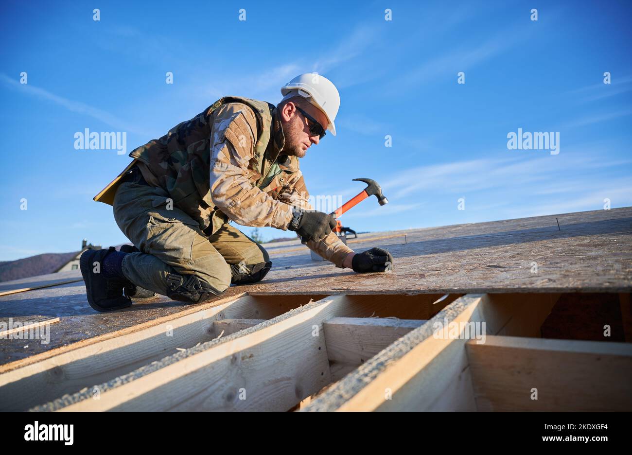 Carpenter hammering nail into OSB panel on the roof top of future