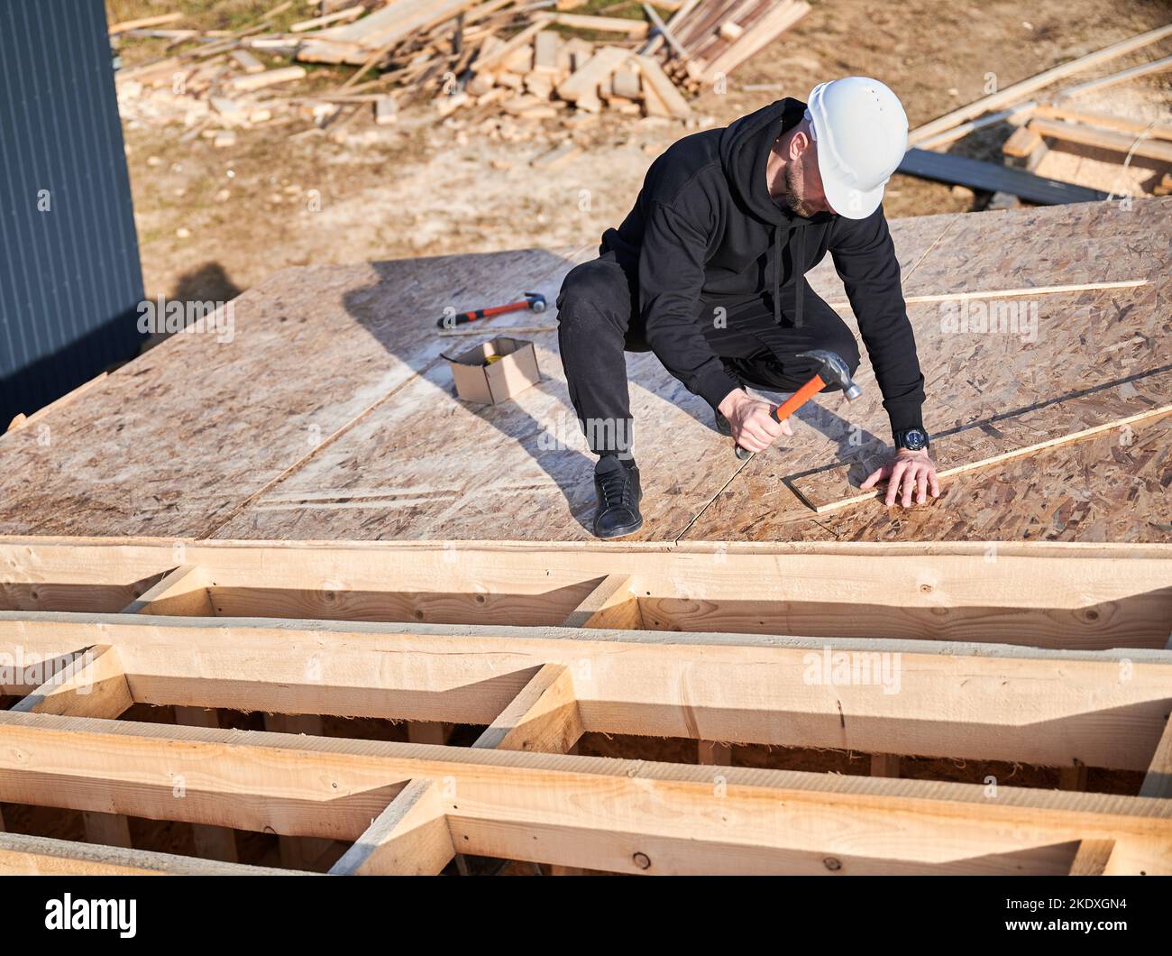 Carpenter hammering nail into OSB panel on the roof top of future