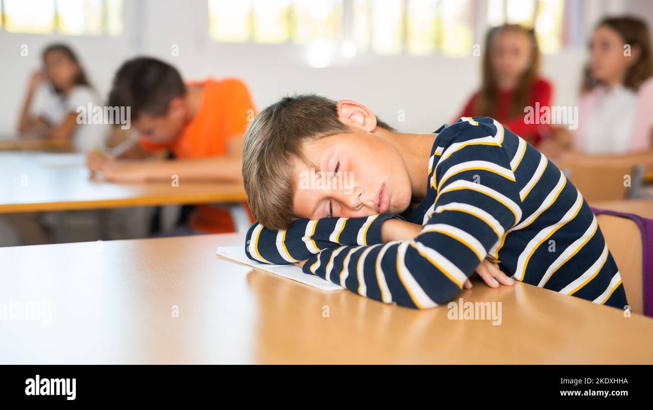 Boy is tired and sleeping at the desk in classroom Stock Photo