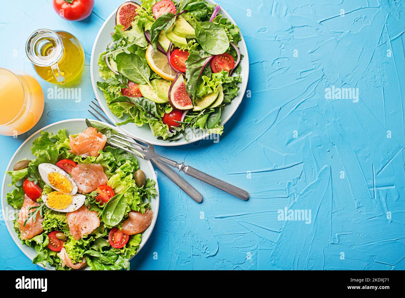 Fresh green lettuce salads with smoked salmon, cherry tomatoes, egg and avocado on blue table background Stock Photo