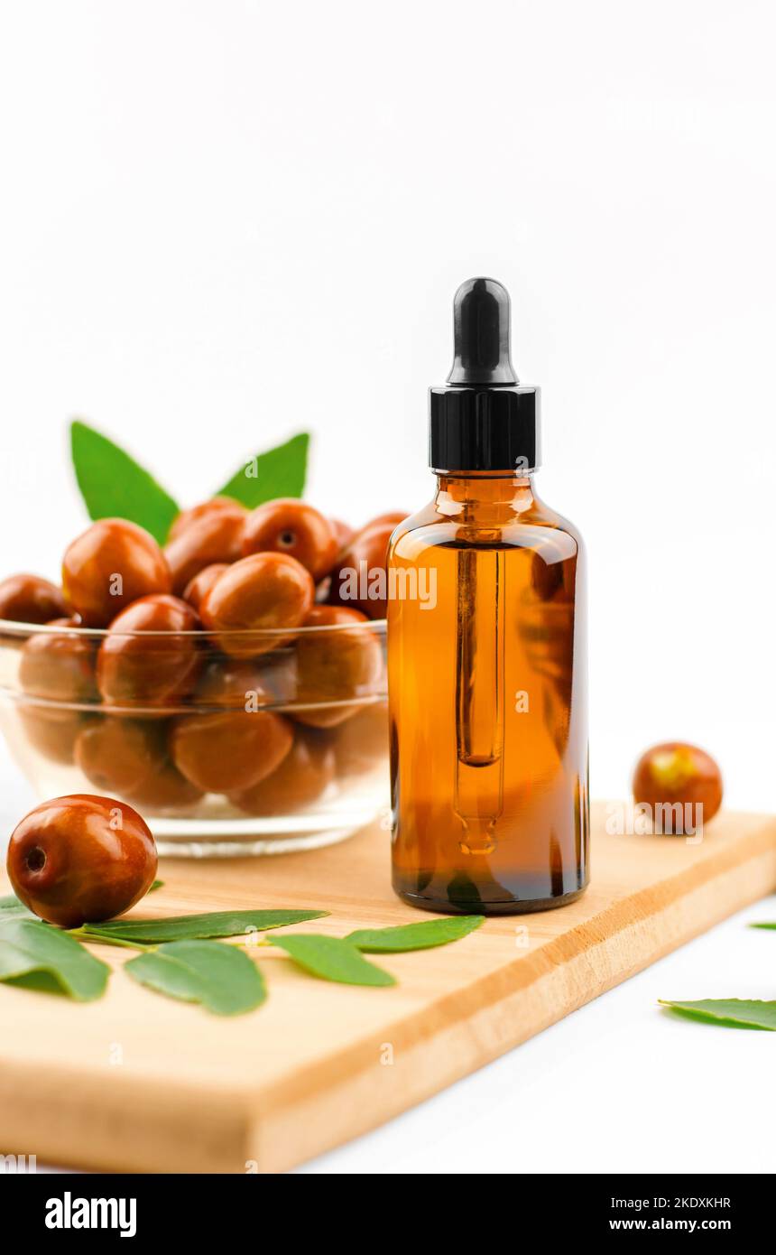 Jojoba oil in a bottle with a dropper on a wooden table with ripe jojoba fruits. Chinese Date Oil and Fruit Stock Photo