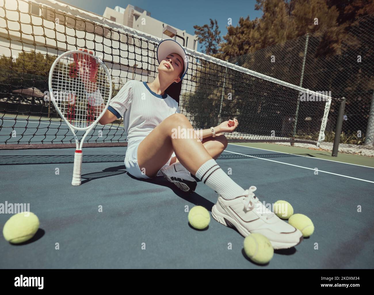 Tennis, sports and exercise with a woman athlete sitting on a court with a racket and balls after a game. Fitness, sport and training with an Stock Photo