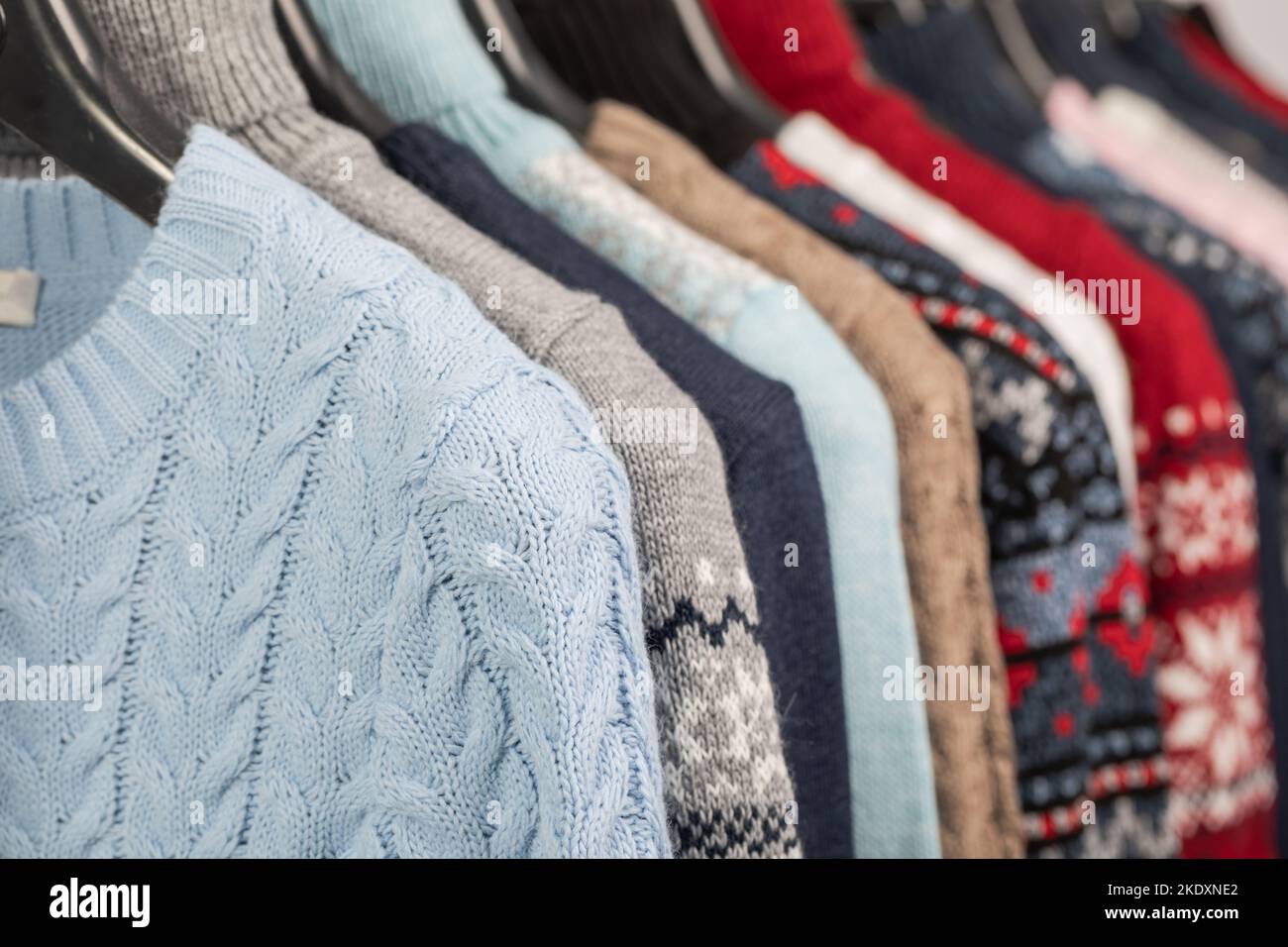 Various vintage sweaters or pullovers on hanger rack in a used goods store. Thrifting and sustainability in clothing concept Stock Photo