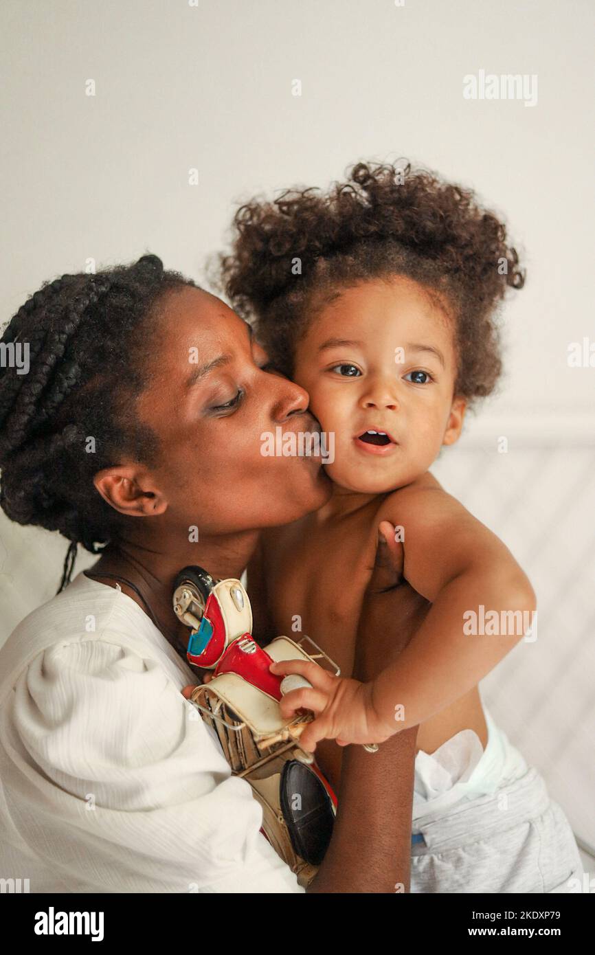 Tender black mother in white dress with cute little girl and kissing