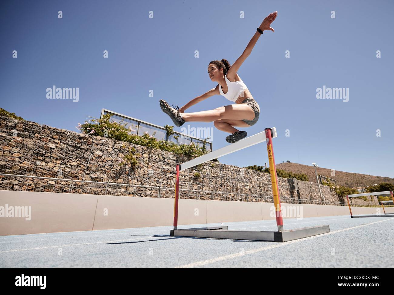 Runner, fitness and girl stadium jump for athlete hurdle training, workout or competition race. Challenge, running and power performance of athletic Stock Photo