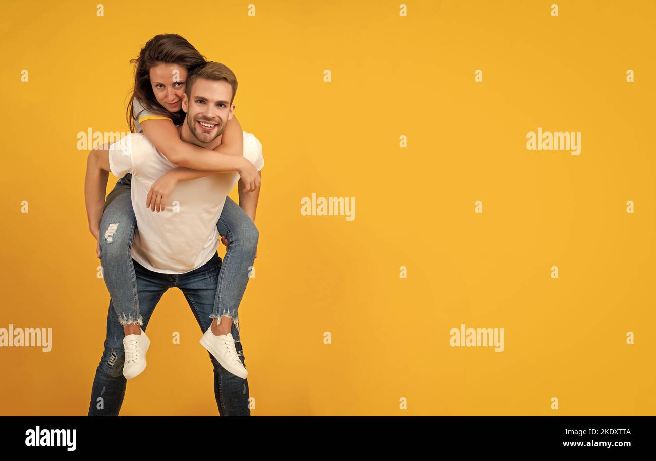 Happy romantic couple having fun doing piggyback ride yellow background ...