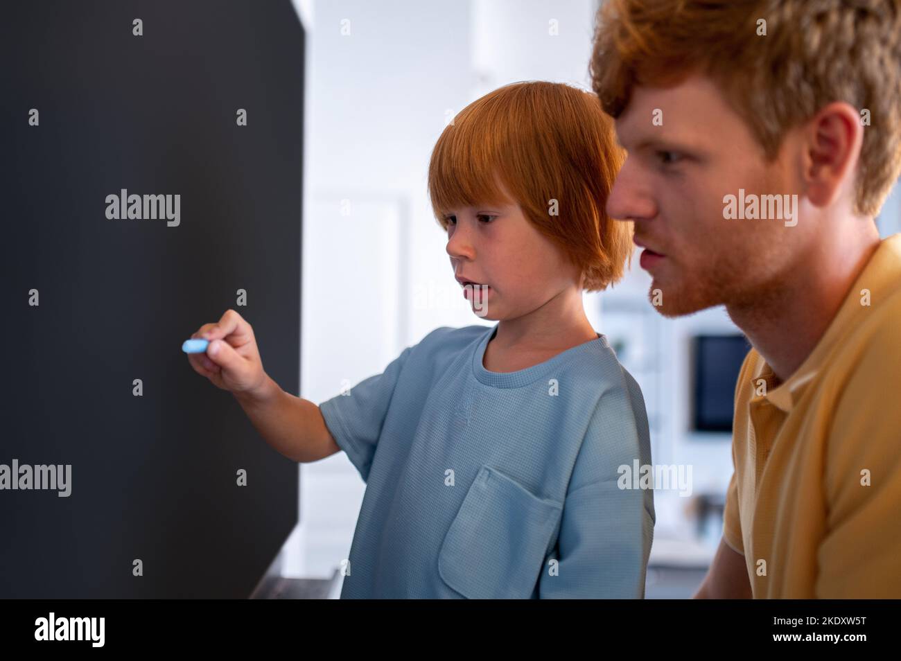 Little boy standing near the blackboard and wtriting something Stock Photo