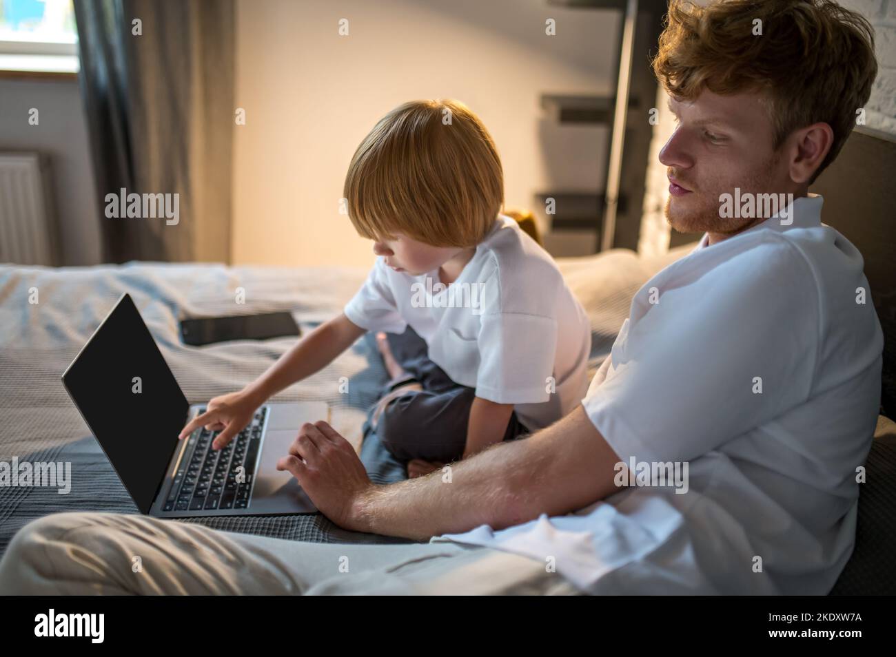 Dad and son lying in bed and watching something online before sleep Stock Photo