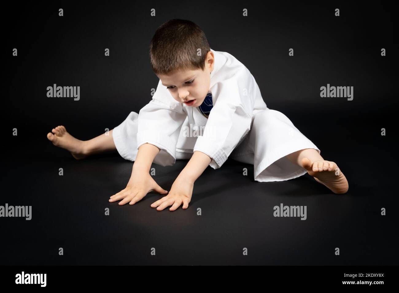 A 5yearold boy practices karate, stretches his legs on a black
