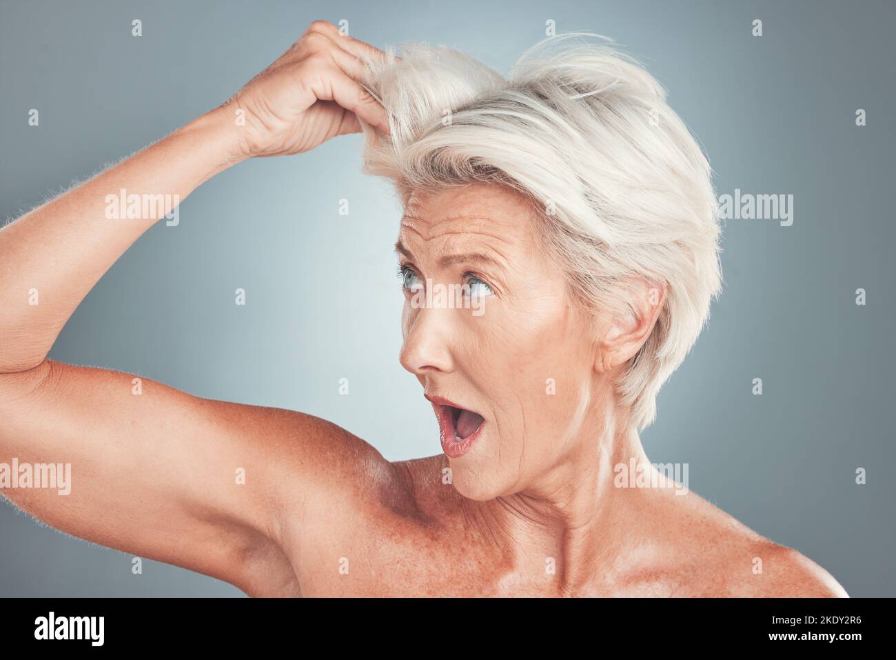 Elderly woman with surprise, white hair in gray background studio and shocked face at healthy haircut. Short hairstyle in senior age, old lady with Stock Photo
