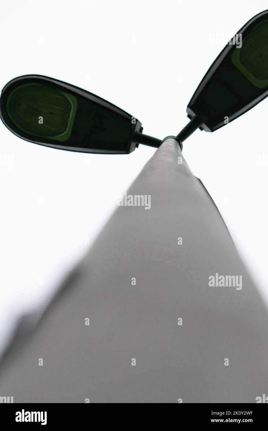Triple street lamp. Grey street lamp from bottom up. Selective focus. No people, nobody. Different angle, composition. Vertical photo. Noise, grain. Stock Photo