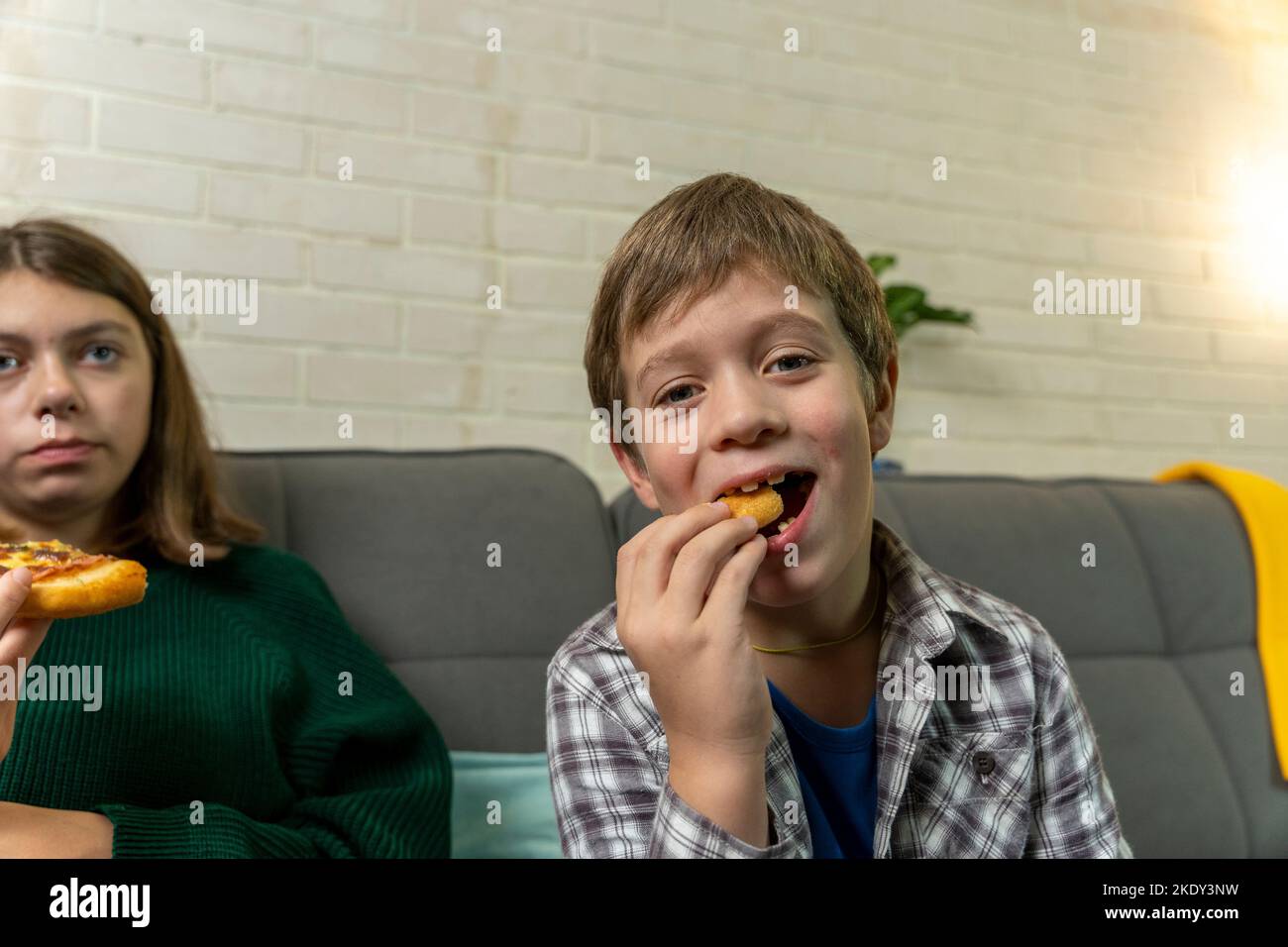 boy is sitting at home on the couch, eating pizza and watching TV Stock