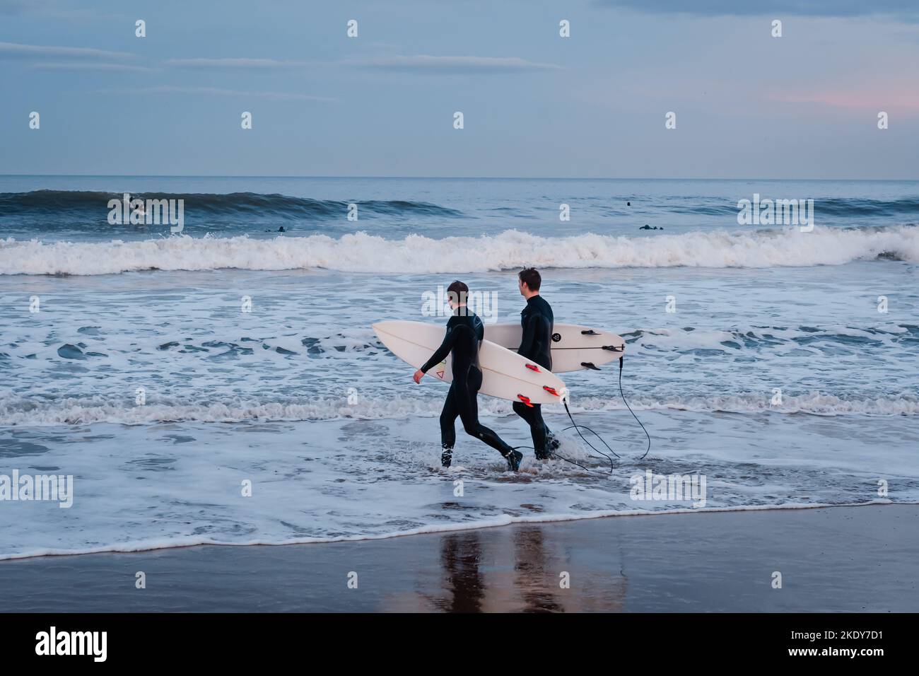 Two surfers walking into the North Sea to surf on Longsands Beach in Tynemouth, North Tyneside, England Stock Photo