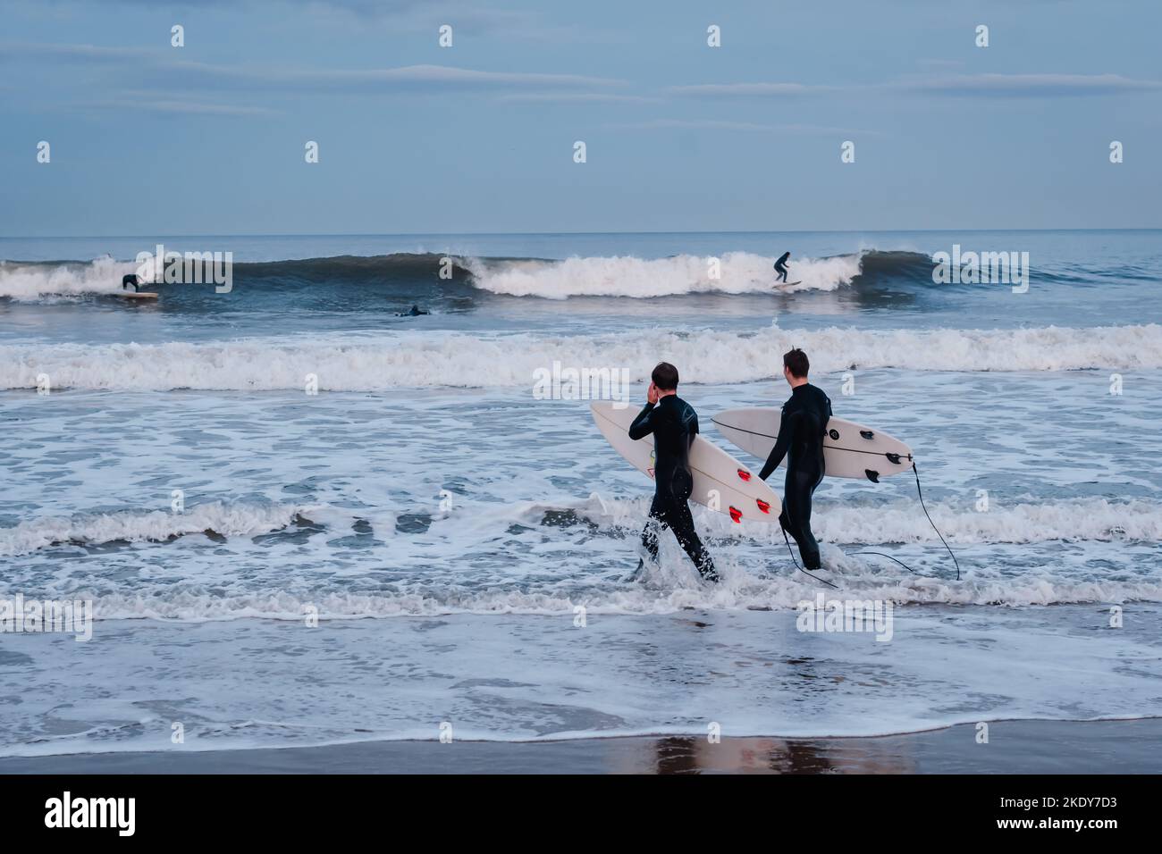 Two surfers walking into the North Sea to surf on Longsands Beach in Tynemouth, North Tyneside, England Stock Photo