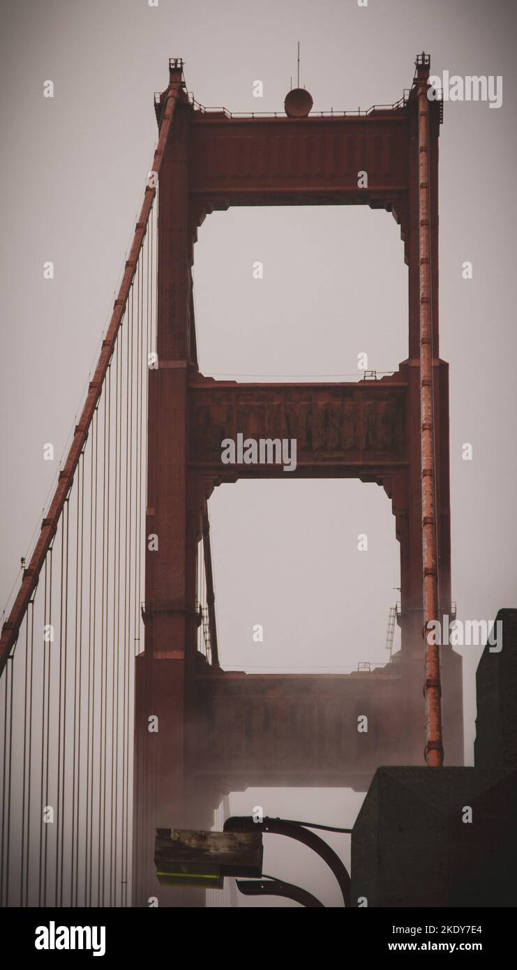A vertical shot of the historic red Golden Gate Bridge under a misty ...
