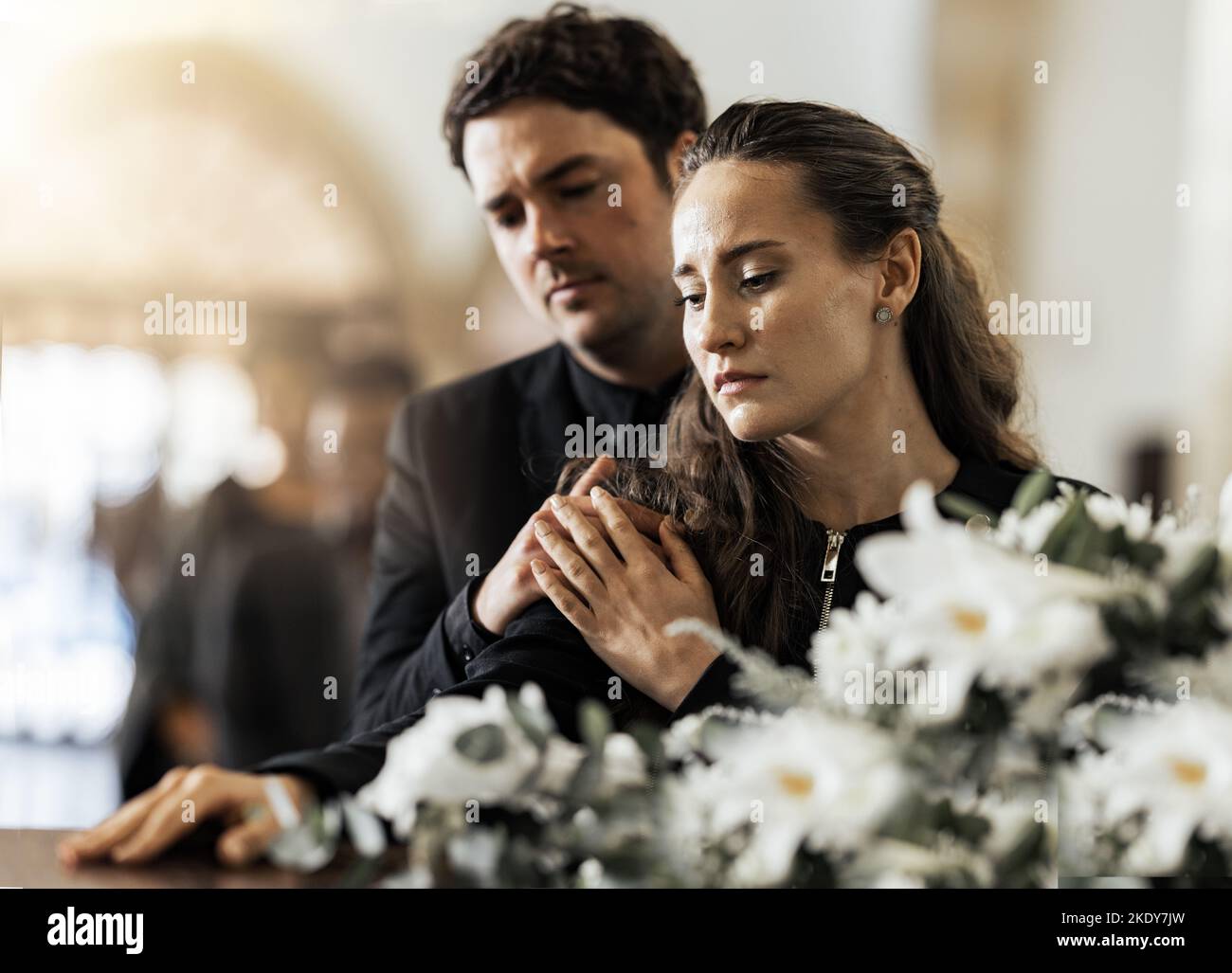 Sad, funeral and flowers with couple and coffin in church for death, respect and mourning. Grief, goodbye and empathy with man and woman loss at Stock Photo