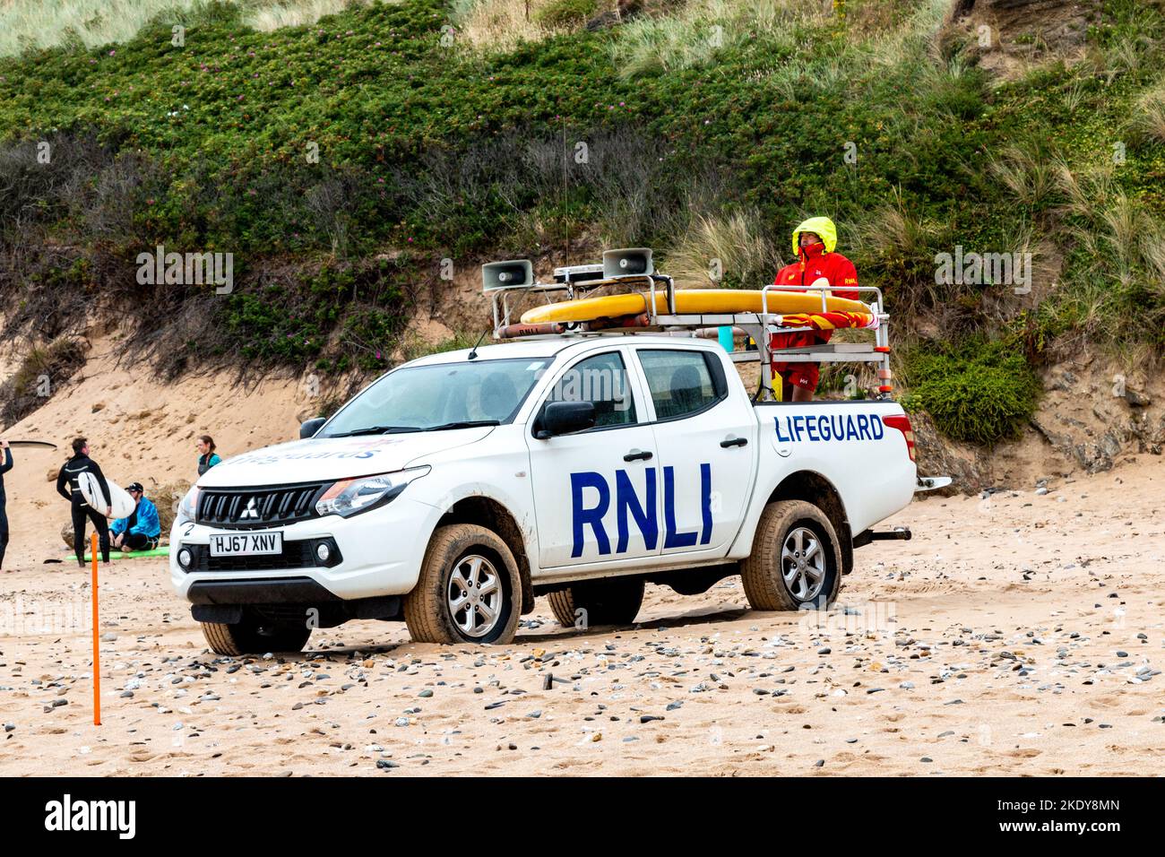 On a cold day the RNLI lifeguard wears a big coat with the hood up while keeping watch from the back of his pick up truck, Fistral Beach, Newquay. Stock Photo