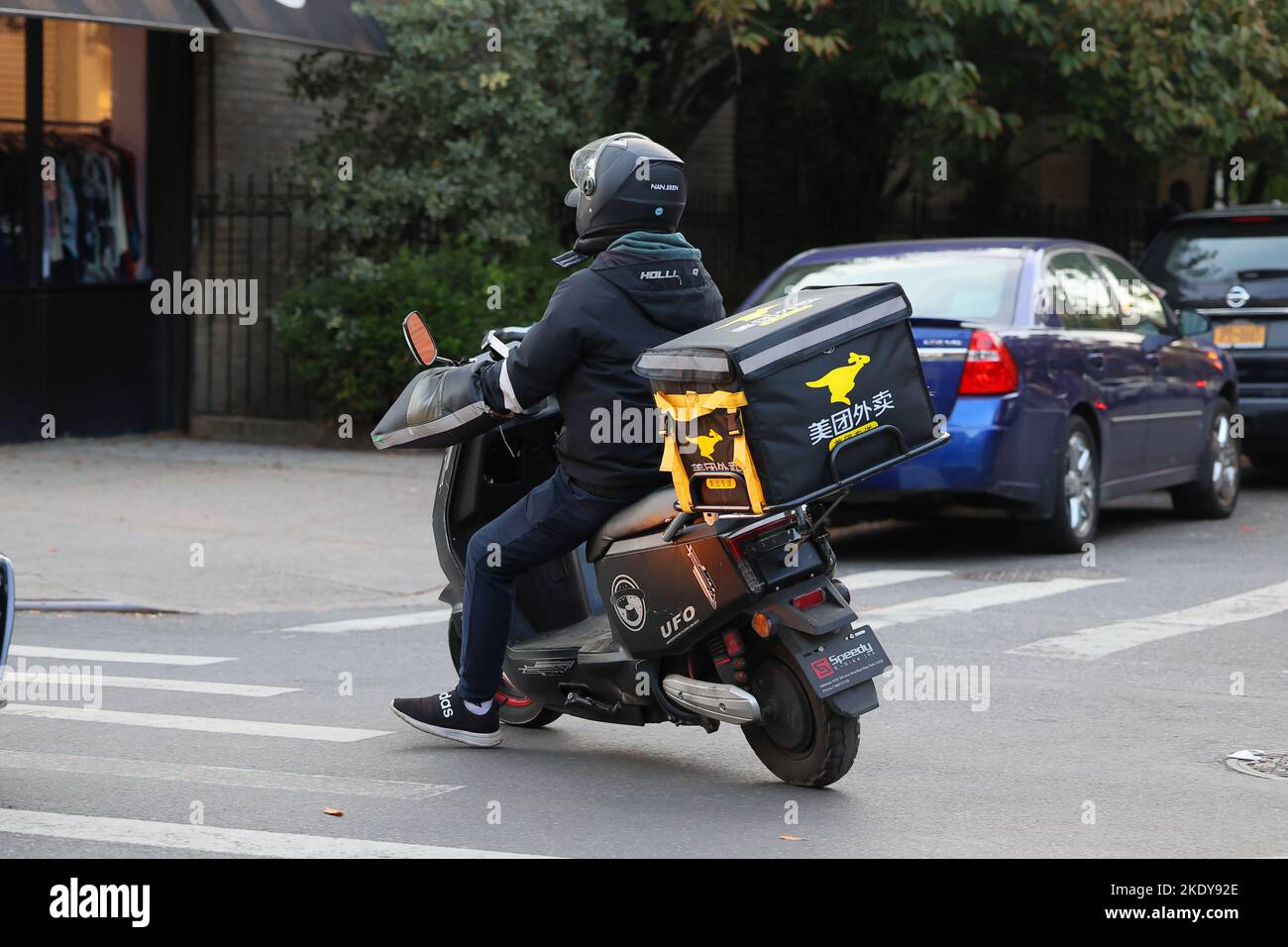 A food delivery person with a Meituan branded insulated bag on an electric moped in Brooklyn, New York. Meituan 美團外賣 Asian food delivery 美团外卖 Stock Photo