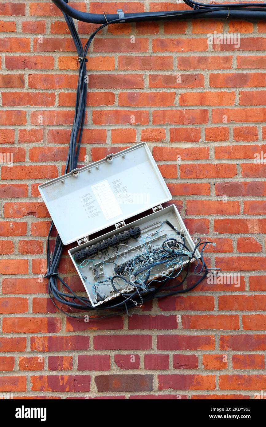 An outdoor telephone box with tangled wires and corrosion, haphazardly dangling off a brick wall. Stock Photo