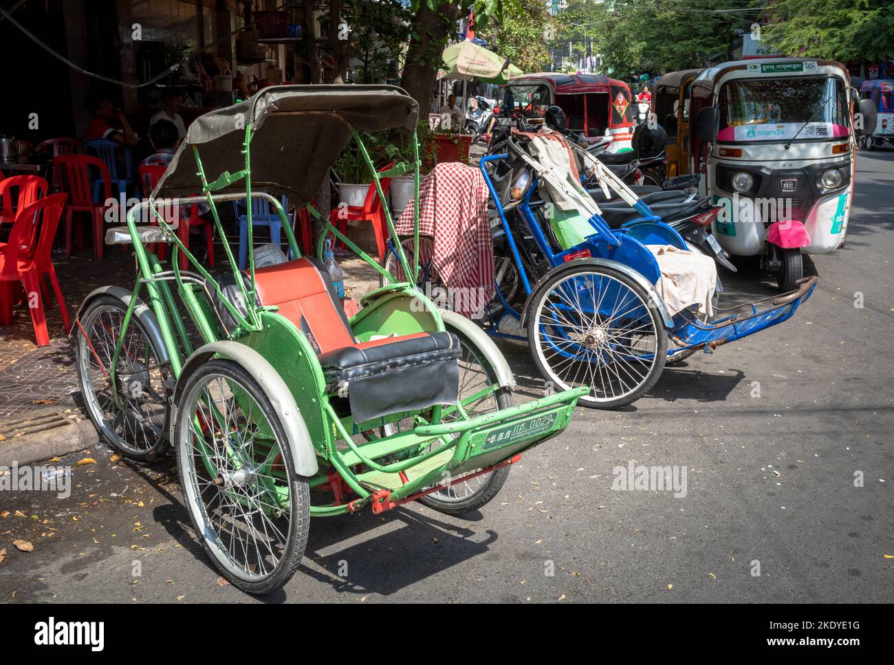 Two traditional cyclos (pedicabs) parked on a pavement next to tuktuks in the centre of Phnom Penh, Cambodia. Stock Photo