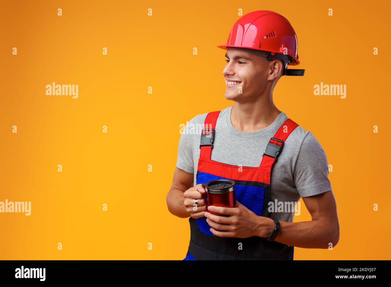 Young builder in uniform holding coffee cup on yellow background Stock Photo