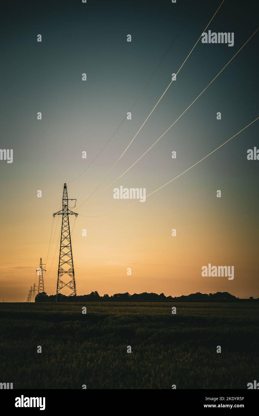 A vertical shot of the silhouettes of transmission towers at sunset ...