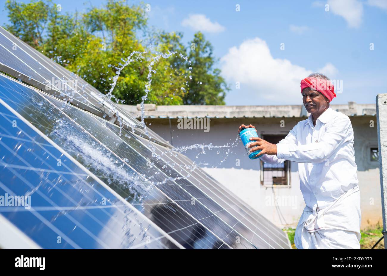 Indain Village farmer cleaning with water on solar panels at farmland - concept of renewable energy, maintenance service and sustainable future Stock Photo