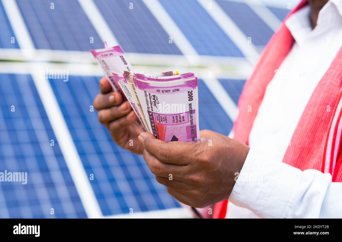 close up shot of farmer hands counting money in front of solar panel - conept of savings, profit making and investment in solar energy for electric Stock Photo