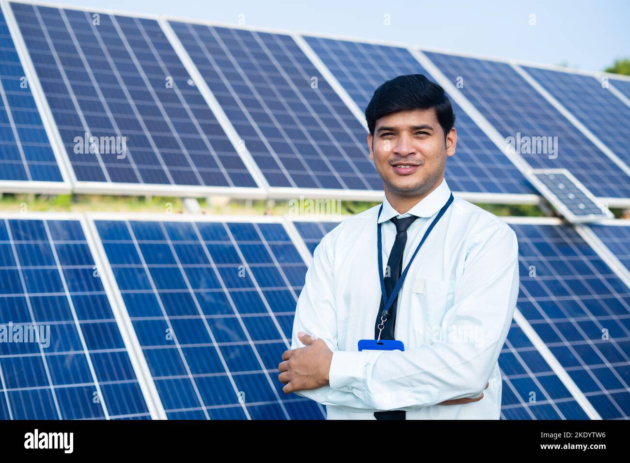 Smiling bank officer standing with crossed arms by looking at camera in front of solar panels - concept of successful, renewable energy and investment Stock Photo