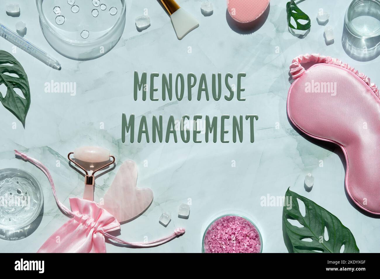 Menopause management text on wellness flat lay. Pink stone facial roller and guasha stone on mint green with monstera leaves. Towel, sleep mask Stock Photo