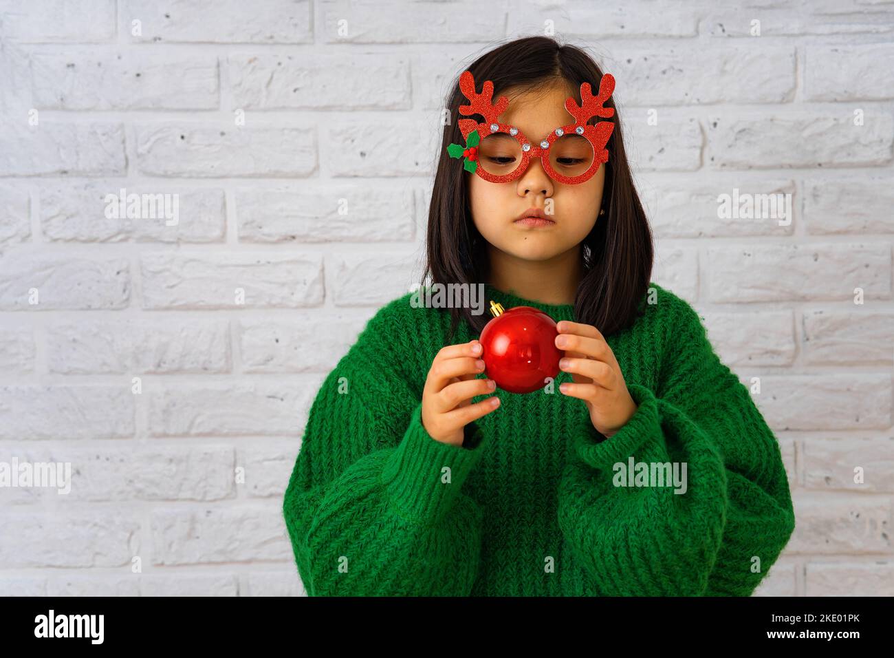 Asian girl in masquerade glasses with reindeer horns, playing with a Christmas ball Stock Photo