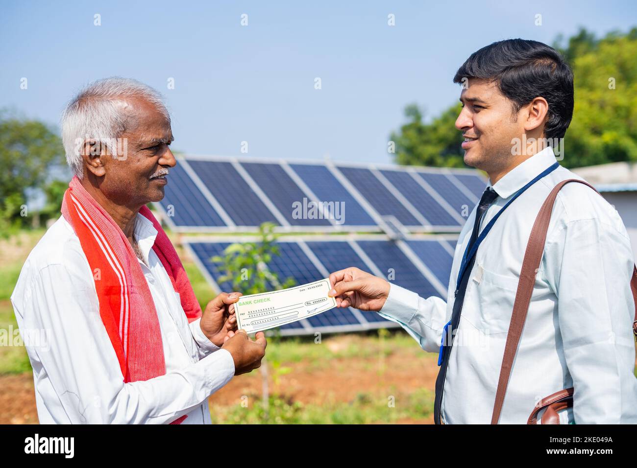 Farmer receiving bank check from banker in front of solar lenal at farmland - concept of finacial, agricultural loan and renewable. Stock Photo