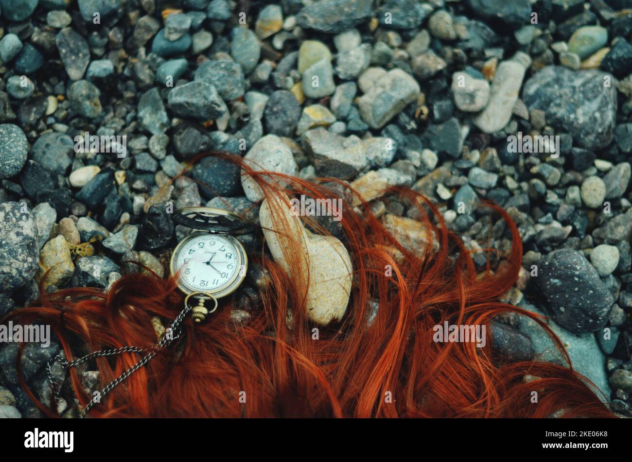 Long red hair and a pocket watch on a rocky beach Stock Photo