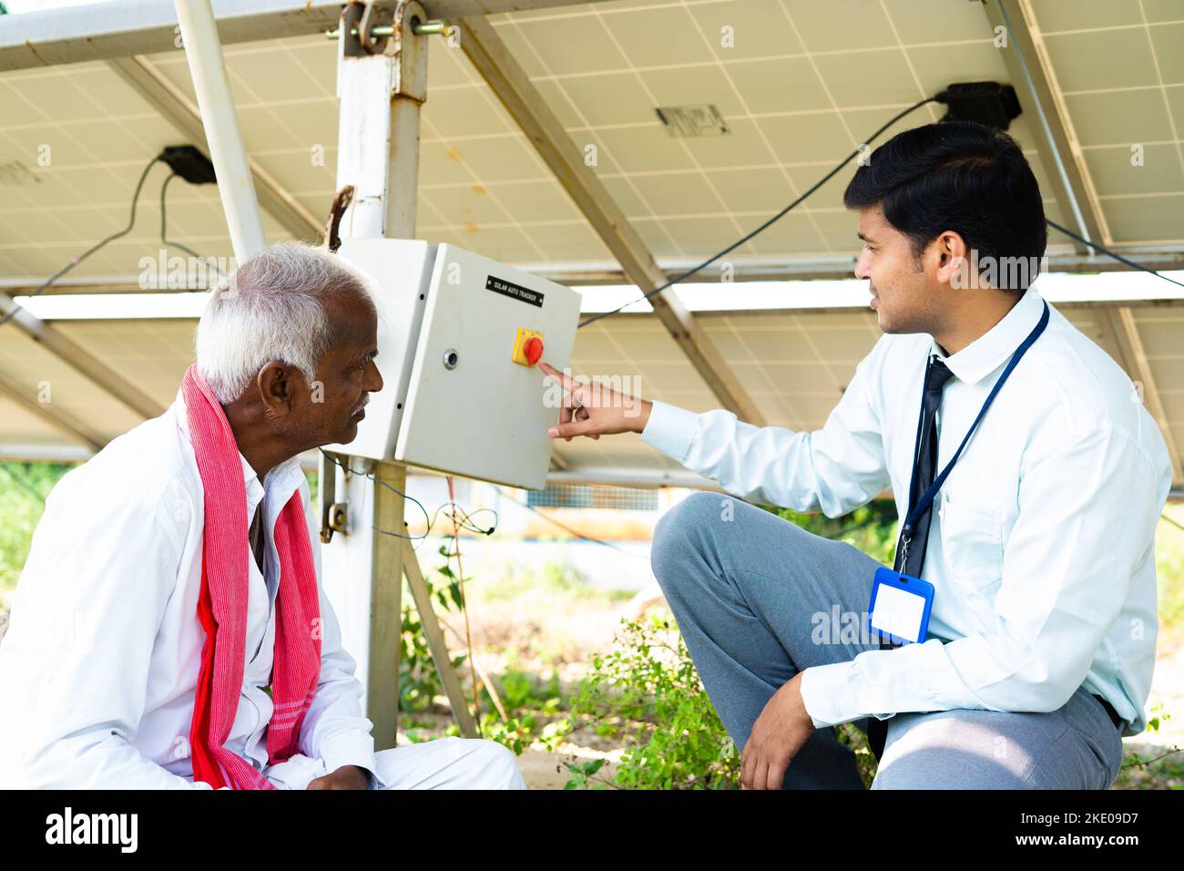 Engineer explaining to Indian farmer about sloar power generation operating below the panel module at agricultural farm land - concept of modren Stock Photo