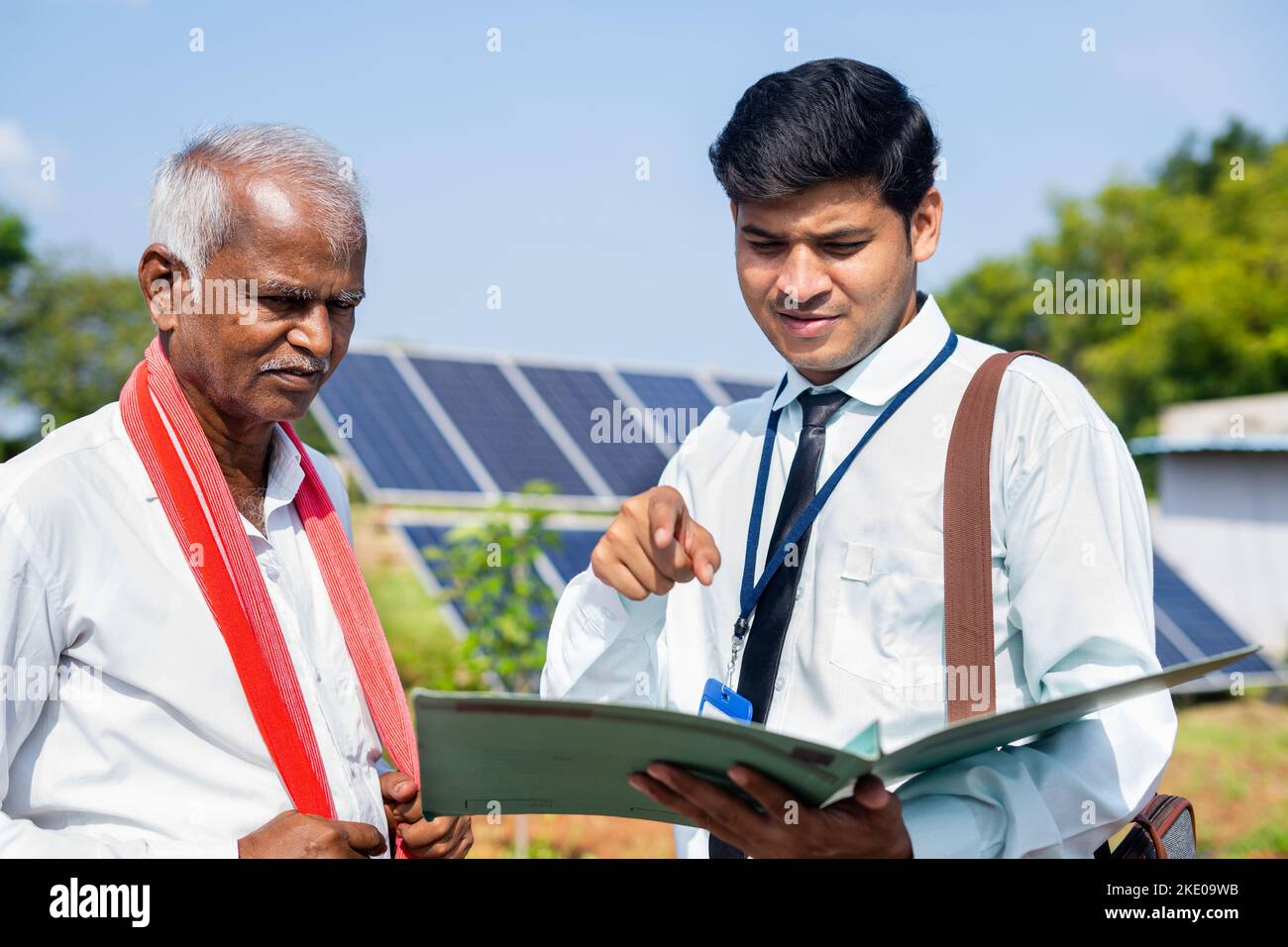 focus on farmer executive or officer checking on loan documents from village farmer in front of solar panel - concept of financial, banking support Stock Photo