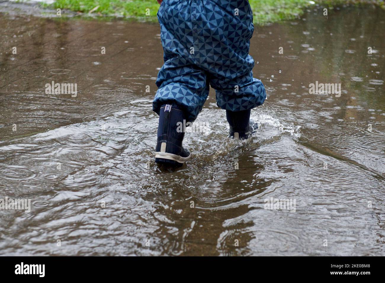 A child walking through a puddle in rubber boots in rain Stock Photo ...