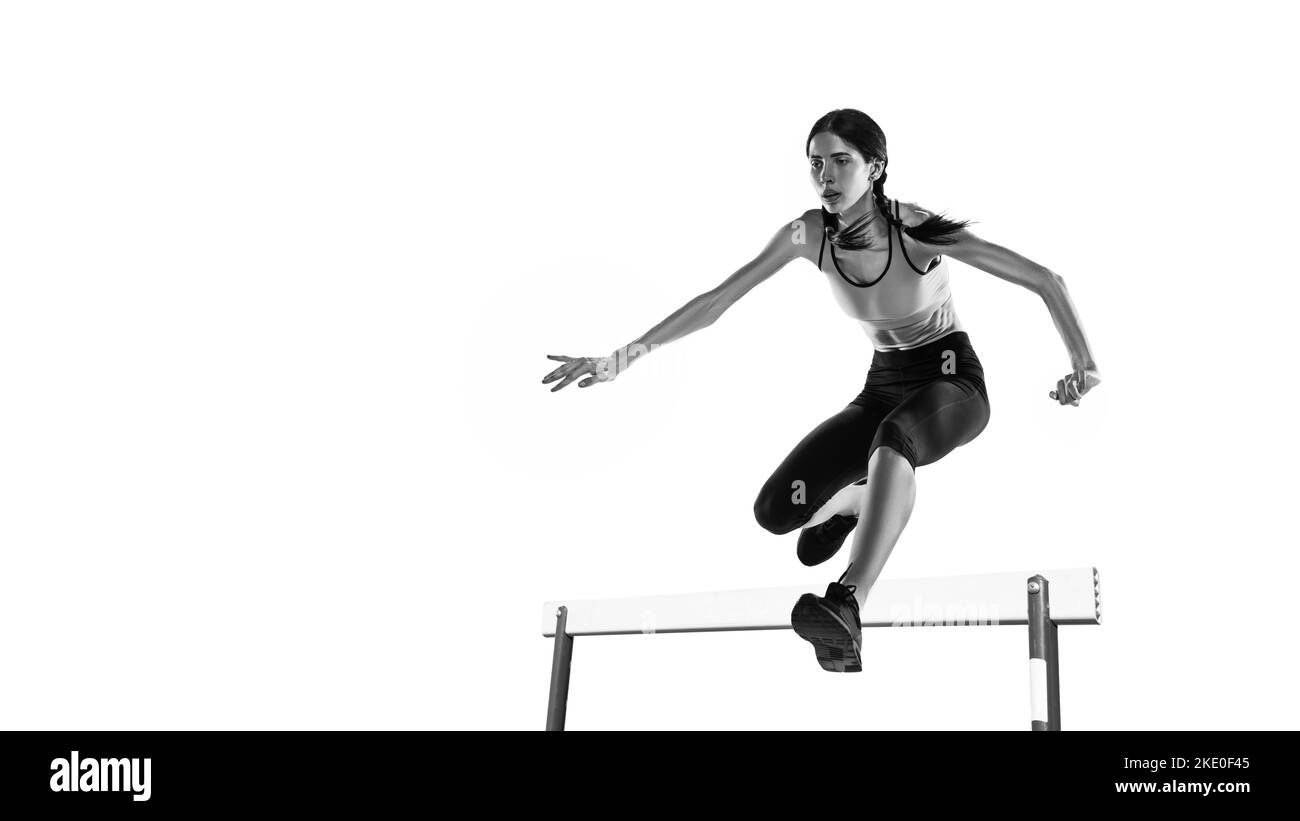 Steeplechase. Black and white portrait of professional female athlete, runner, jogger in action isolated on white background. Monochrome. Sport Stock Photo